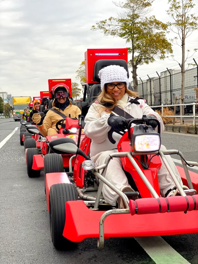 Front rider in white coat and knit hat steering a red go-kart, with others in line behind.